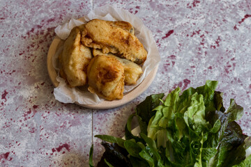 Fried battered cod with salad on the pink background.