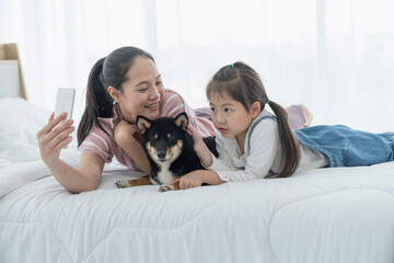 A mom and daughter take a selfie  with a Shiba Inu dog on the bed. Japanese dog.