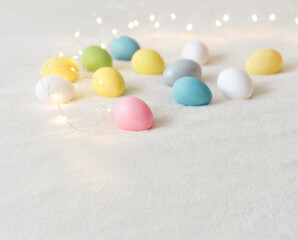 Colored eggs on a light background with garland lights in the Easter holiday.