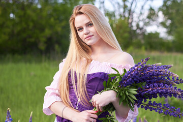 Young attractive long-haired blonde with a bouquet of lupins among a purple field. The concept of...