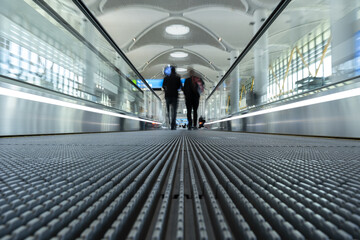 two blurry out of focus people walking on sidewalk people mover in an airport