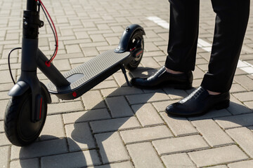 Close-up of a man's feet in a business suit and shoes near an electric scooter