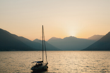 Silhouette of a moored sailing yacht against the background of the setting sun over the mountains. Fiery yellow sunset over the mountains in the Bay of Kotor in Montenegro.