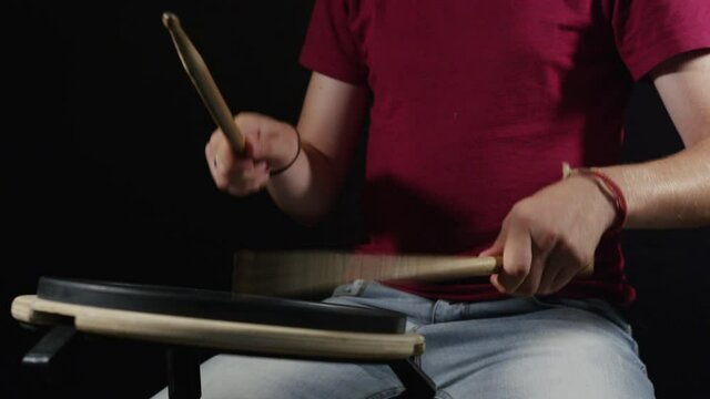 A young caucasian male drummer in red t-shirt practicing on his silent drum pad. 