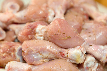 Raw chicken legs sprinkled with spices lie in a heap