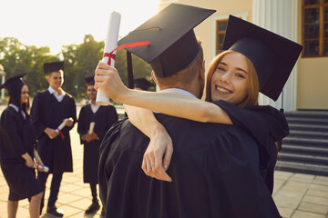 Young happy couple university graduates in traditional bonets standing with diplomas and hugging...