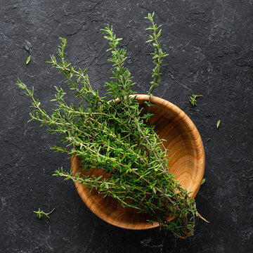Bunch of fresh thyme in a wooden bowl on a black background.