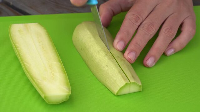 Closeup view 4k stock video footage of woman cutting fresh young squash zucchini vegetable isolated on green plastic chopping board background