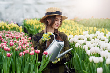 Happy smiling teenager girl in hat with watering can in blossoming tulip garden