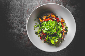 Vegetarian vegetable salad with mushrooms, arugula, tomato, beans and pepper in a bowl on Dark grey black slate background
