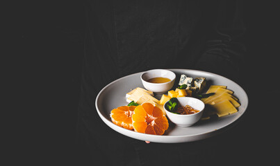 chef in a black suit holds in his hands Cheese plate on Dark grey black background