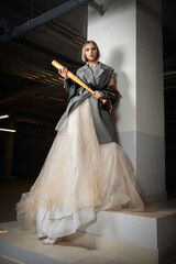 girl teenager blonde in a fluffy skirt with a bat in her hands against a white wall in the basement