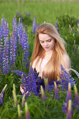 Young attractive long-haired blonde with a bouquet of lupins among a purple field. The concept of nature and romance.