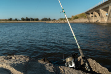 Fototapeta na wymiar Fishing rod with reel piled on the rocks at the side of a river