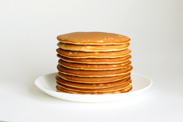 Many pancakes are stacked one on one in a white plate.