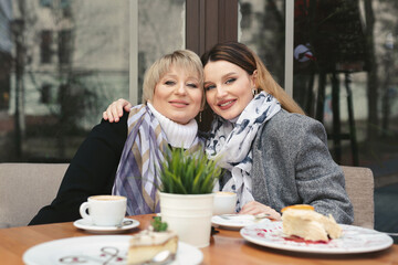 Family day. An elderly woman and her adult daughter drink coffee in a cafe on the sidewalk and hug. Family portrait