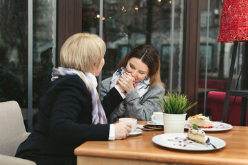An adult daughter kisses her mother's hand and smiles. Emotions of relatives in the cafe
