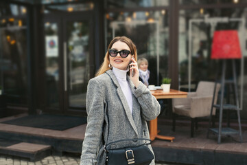 Beautiful young woman in sunglasses is talking on the phone while her elderly mother is waiting in...
