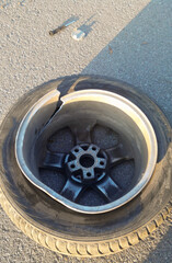 On the asphalt lies a wheel from a car with a split alloy wheel, smashed in a hole on the road