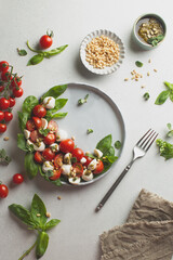 Classic italian caprese salad in grey ceramic plate with fresh tomatoes,mozzarella,basil,pine nuts,pesto and fresh oregano.Foodstyling.Top view with copy space.