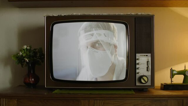 An old analog TV showing a doctor or a scientist in PPE looking at the camera.