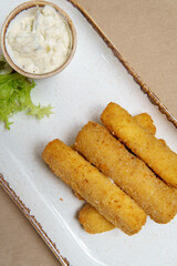 Cheese sticks fried in breadcrumbs. Mozzarella cheese sticks on a plate with sauce and lettuce.