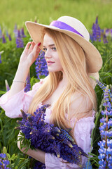 Young attractive blonde in a straw hat with a bouquet of lupins, among a purple field. The concept of nature and romance.