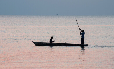 Silhouettes of fishermen sailing in a wooden boat at sunset in Zanzibar.