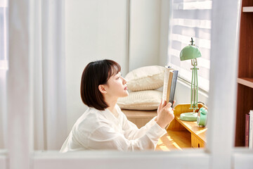 close-up of Asia Korean woman's hands with a cup of coffee, the sun's rays shine through a window in the room. reading  a book on the desk. Hand and book.