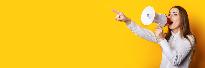 Young woman in a white shirt makes an announcement in a megaphone and points a finger on a yellow...