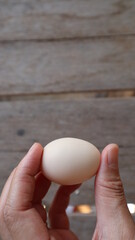 Fototapeta na wymiar Egg in hand. Brown wooden board background for many kinds of cooking.