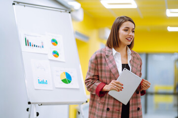 A beautiful business woman is presenting a report / presentation to her business colleagues in a conference room, she is showing a graphics. Serious female employee with flip chart at presentation.
