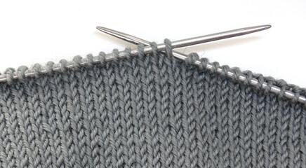 Knitting on knitting needles. Gray woolen fabric on knitting needles on a white background