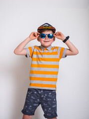 Cute stylish little guy in trendy sunglasses and striped yellow shirt posing with his skateboard against a white wall with copyspace