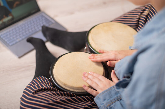 A faceless woman sits on the floor at home and watches educational videos of playing mini bongs. Girl remotely learns to play traditional ethnic drums.