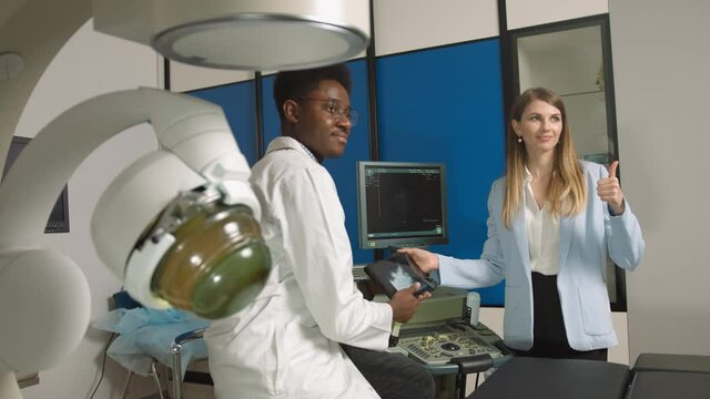 Portrait of smiling pretty woman, posing to camera, while visiting her African man doctor in modern clinic, holding digital tablet with ultrasound scan. Lithotripsy therapy and ultrasound