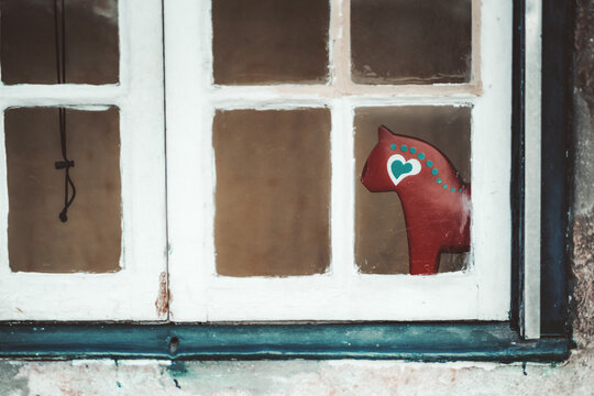 An old stained-glass wooden window of an antique house with a selective focus on the reddish horse or cat children's toy with teal circles pattern and a heart behind the glass, shallow depth of field