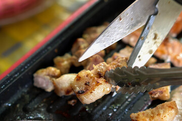 Korean BBQ pork, Use Food tongs and shears to cut grilled pork belly.