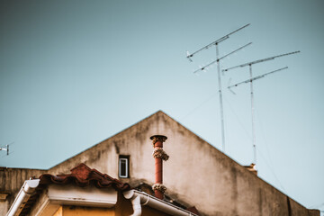 A triangle roof of an old house with multiple tv antennas, shallow depth of field with a selective focus on the small chimney in the foreground wrapped in Christmas tinsel, small window, clear skies