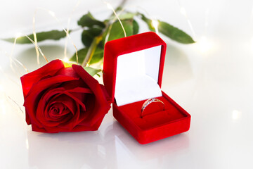 A gold ring in a red velvet box as a gift or engagement, wedding, next to a red rose and burning...