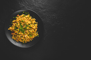 Bulgur with vegetables and meat on black plate on Dark grey black slate background