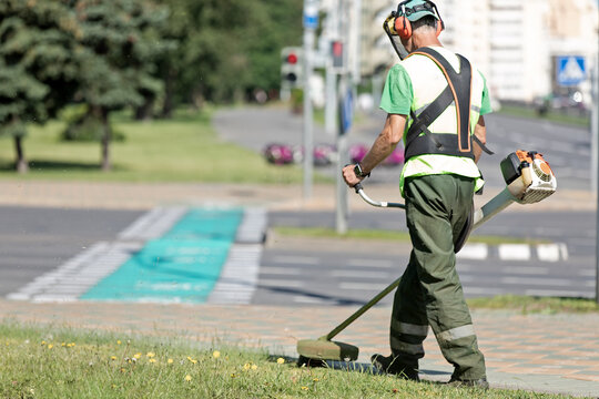 Road landscaper man worker cutting grass along city street