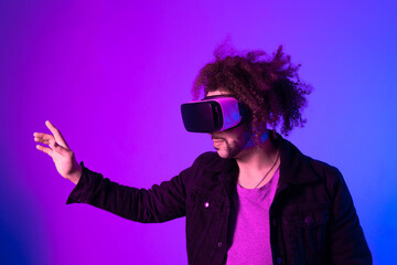 Surprised young man with afro hair touching the air and smiling during VR experience. Horizontal shot in studio. purple blue background