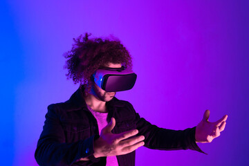 Surprised young man with afro hair touching the air and smiling during VR experience. Horizontal shot in studio. purple blue background