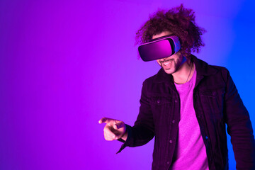 African american man long afro hair with vr glass, playing video games with virtual reality headset, trying to touch something with his hand. pink blue background