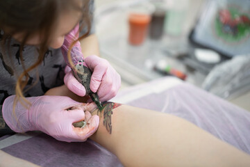 Close-up of a female artist making a color tattoo on the leg of a young girl. Tattoo artist stuffs a ladybug on a girl's leg, tattoo for a girl
