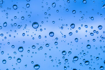 blue rain water drops on a window glass close up , colored drop background macro in a blue light