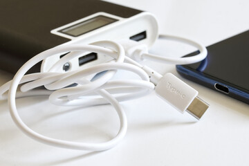 Large and capacious power bank with monitor, cable and usb type-c connector lies on a white surface next to the smartphone. The concept of recharging modern gadgets. Macro