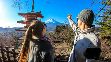 Obraz na płótnie Canvas A couple standing next to Chureito Pagoda, Japan and pointing at Mt Fuji in the back. They are having a lot of fun, exploring and enjoying beautiful landscape. Holly mountain. Clear and sunny day.