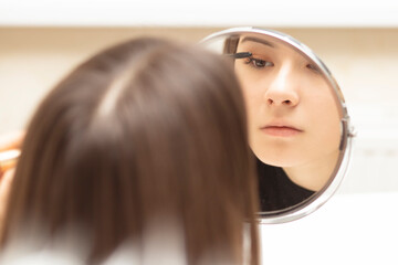 Fototapeta premium Teen girl applies makeup while looking in the mirror